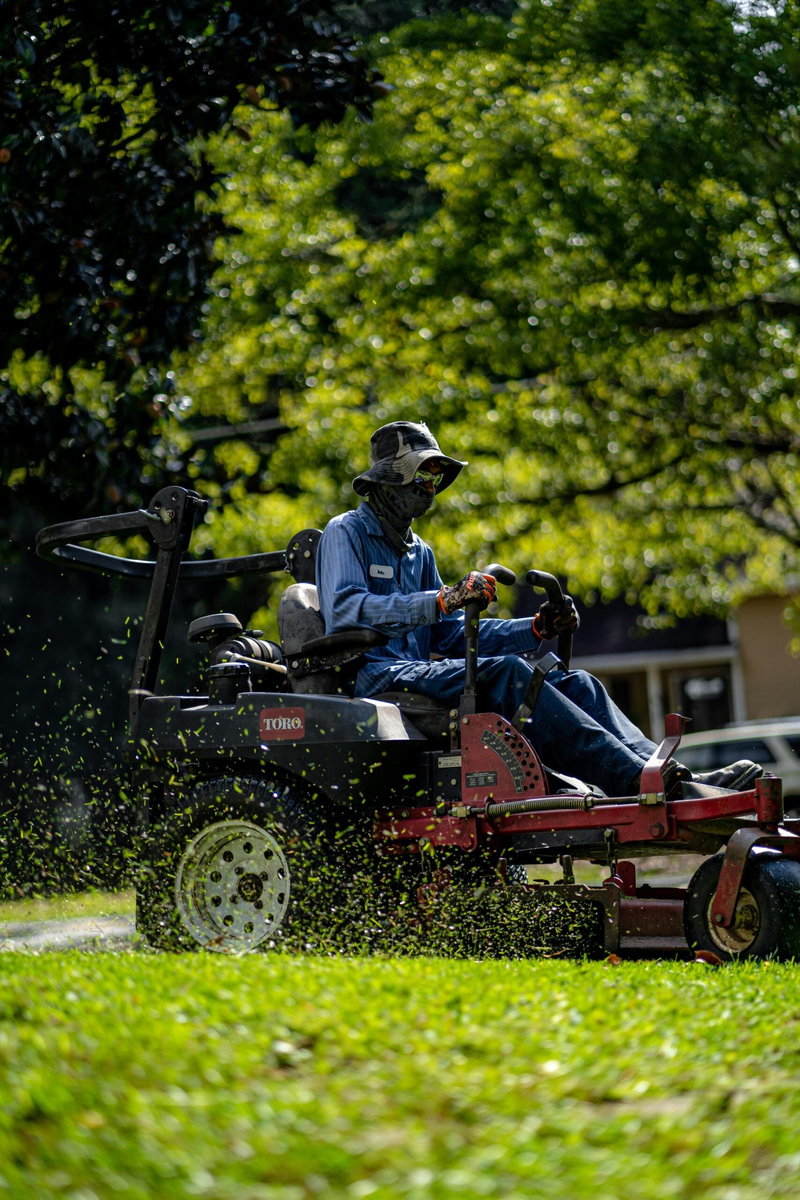 Person on a lawn mower cutting grass in a sunny, green park.